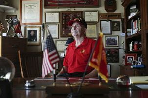A veteran sits at his desk surrounded by military awards and memorabilia