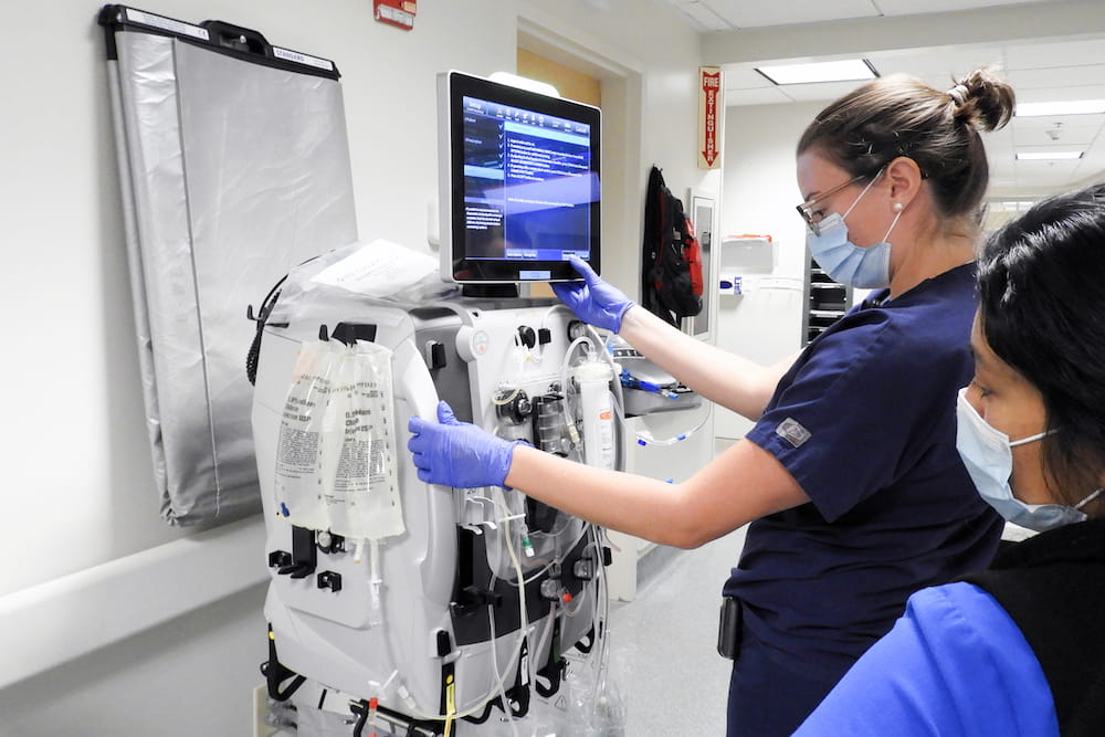   Continuous Renal Replacement Therapy RN educator, Erin Glikes sets up the SB-101 device containing mesenchymal stem cells in series with the Baxter PrisMax dialyzer., while medical ICU nurse Jessie Ramirez looks on. Photograph by Natalie Wilson.