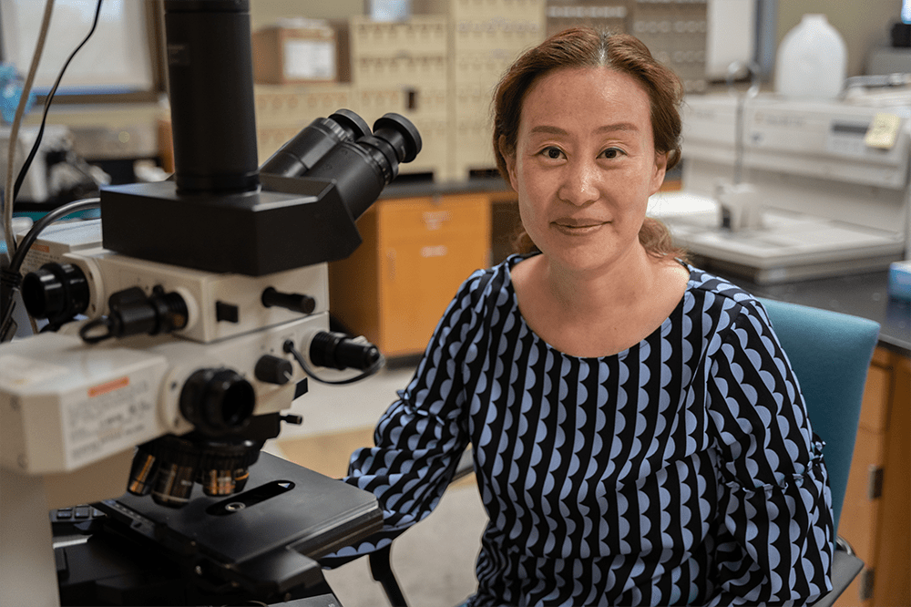 Angela Yoon, D.D.S., sits beside a microscope.