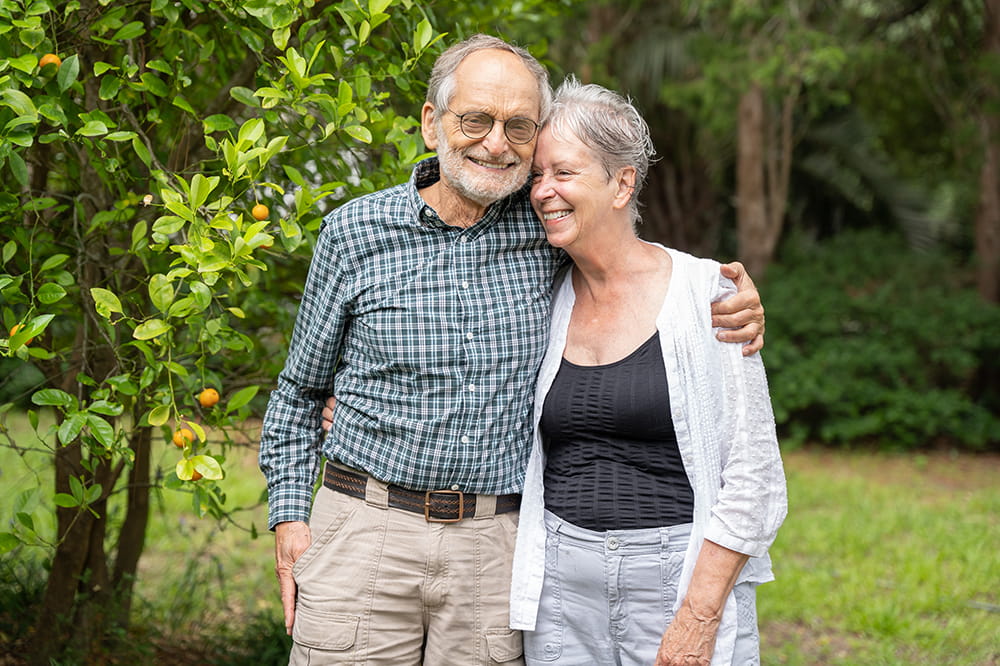 An older man and woman lean into each other affectionately in a garden