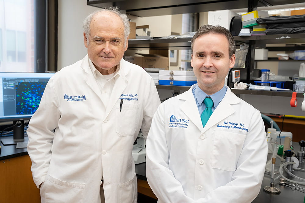 two men in white lab coats pose in a lab