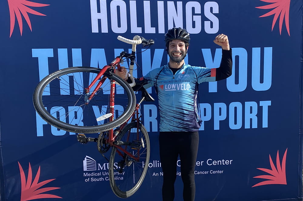 man holds up bike triumphantly in front of sign that says Hollings thank you