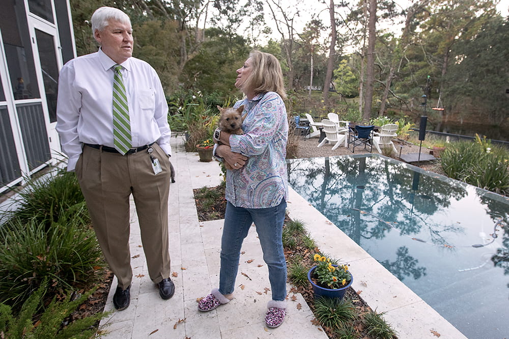 Cole and his wife, who is holding their dog, talk outside by pool