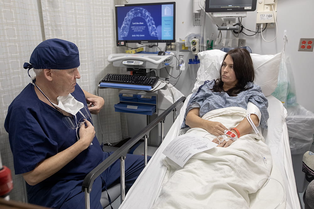 Cole sits by a woman's bed, explaining to her the surgical procedure that he's about to perform on her