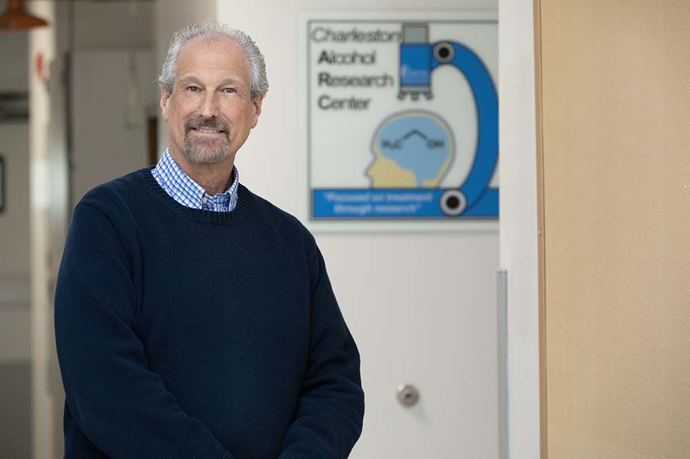 Man wearing a navy sweater stands by a picture of a microscope.