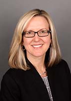Smiling woman with blonde hair and glasses wearing a black jacket.
