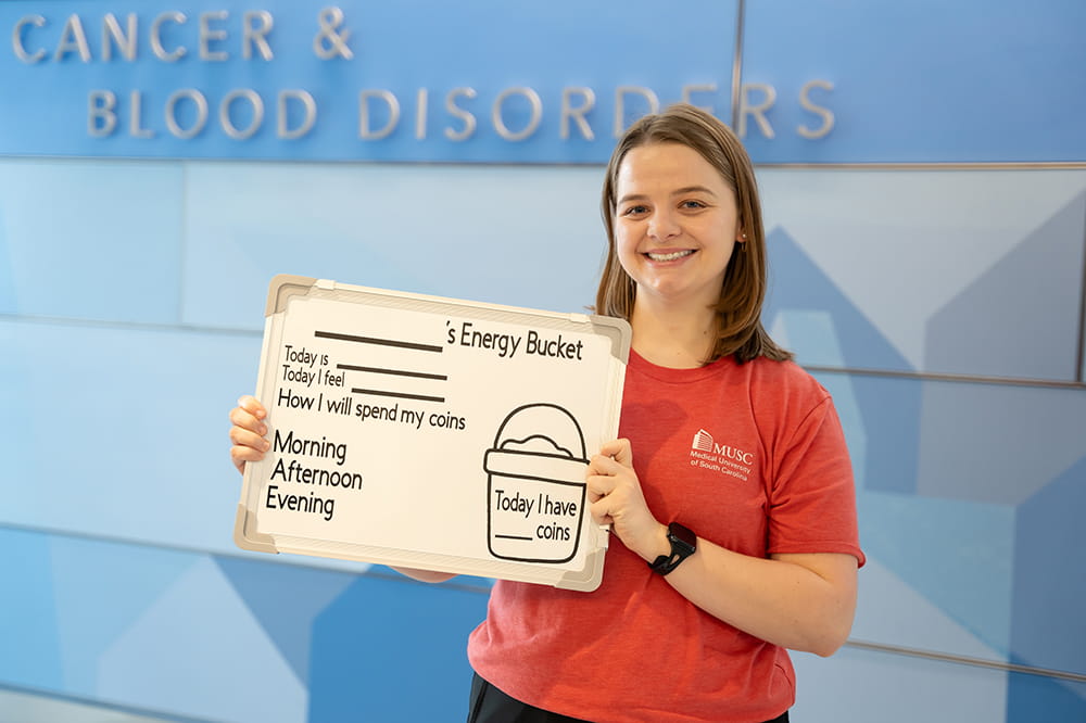 OT student Maddie Gies holds up a white dry erase board that pediatric cancer patients can fill out to indicate fatigue levels