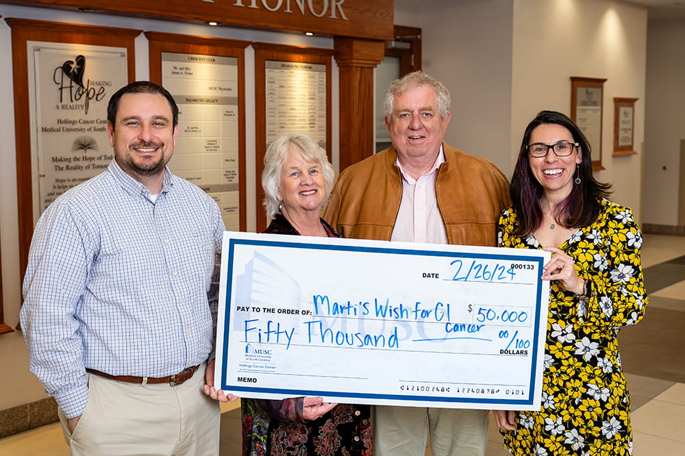 four people stand in the Hollings lobby holding an oversized check for the Marti's Wish fund