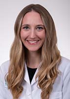 Smiling woman with long blonde hair wearing a white medical coat.