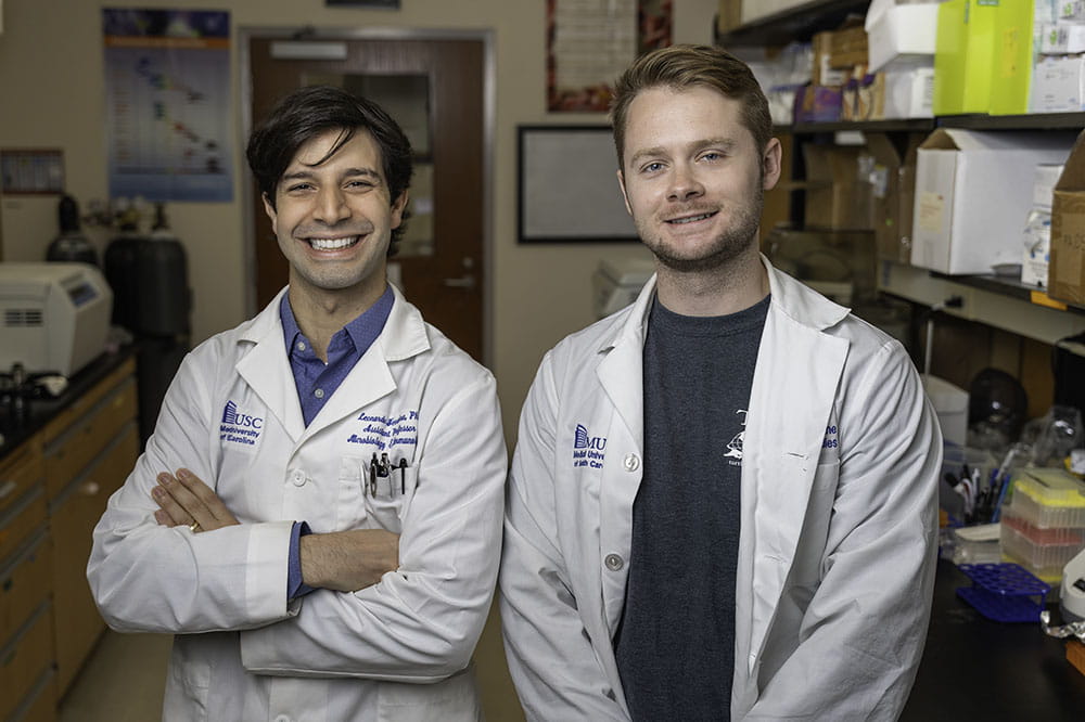 two men in white lab coats pose in a lab at Hollings Cancer Center