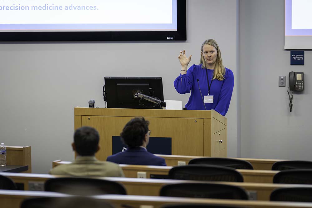 A blonde woman wearing a blue top gestures as she speaks from behind a podium.