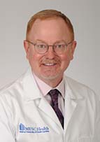 Headshot of a man with short hear and a goatee wearing glasses and a white doctor's cost.