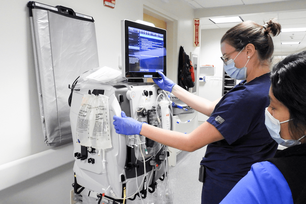 Continuous renal replacement therapy RN educator Erin Glikes sets up the SB-101 device containing mesenchymal stem cells in series with the Baxter PrisMax dialyzer, while medical ICU nurse Jessie Ramirez looks on. 