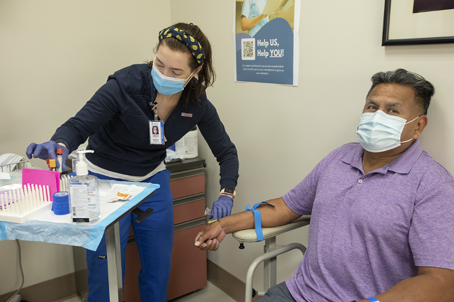 Nurse Katherine Anderson draws blood from Argentino Calvo during his appointment for the Novavax vaccine trial through MUSC.